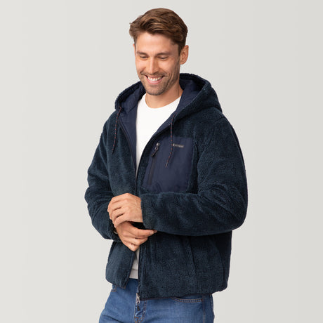 [Matt is 6'2" wearing a size Medium.] Men’s Free Country reversible quilted jacket in navy with zip-front closure, adjustable drawstring hood, and dual hand pockets—flips to plush sherpa interior for added warmth and comfort. Styled with a white crewneck shirt and jeans for a casual, cold-weather look.