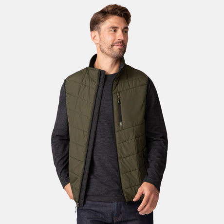[Matt is 6'2" wearing a size Medium.] Man wearing the Free Country Men's FreeCycle® Stimson Puffer Vest in green, featuring quilted design, REPREVE® poly fill, and a vertical zip, layered over a black long-sleeve shirt with dark jeans.