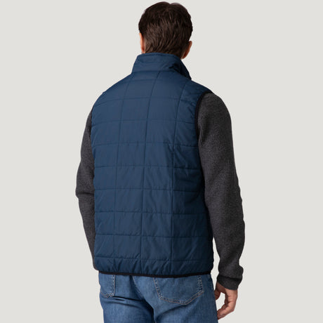 [Vince is 6’1” wearing a size Medium.] Man wearing the Free Country Men's FreeCycle® Stimson Puffer Vest in navy, featuring quilted design, REPREVE® poly fill, and a vertical zip, layered over a burgundy long-sleeve shirt with dark jeans.