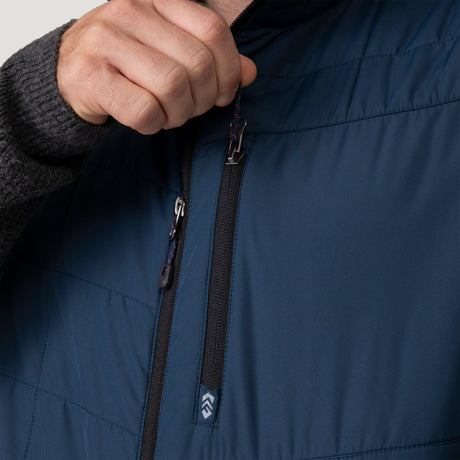 [Vince is 6’1” wearing a size Medium.] Man wearing the Free Country Men's FreeCycle® Stimson Puffer Vest in navy, featuring quilted design, REPREVE® poly fill, and a vertical zip, layered over a burgundy long-sleeve shirt with dark jeans.