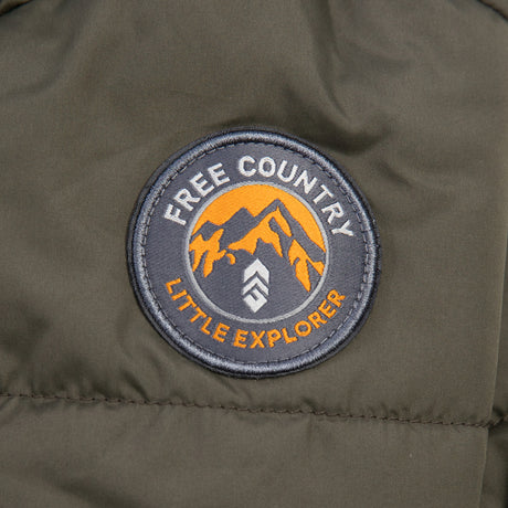 A circular patch on dark fabric features orange mountains, "FREE COUNTRY" at the top, "LITTLE EXPLORER" at the bottom, and a chevron—perfect for the Free Country Kids' Infant Lightweight Quilted Puffer Snow Suit with cozy recycled polyfill and sherpa lining.