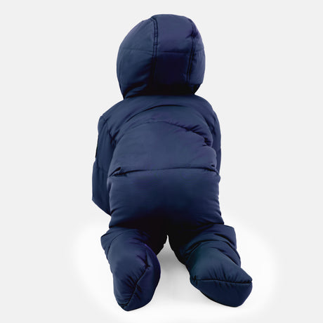 A baby wearing the Clearance Kids' Out of Bound Puffer Snow Suit in dark blue crawls on a white surface, back to the camera. The sherpa-lined hood and double zipper keep their padded hands and legs warm in this recycled polyfill snowsuit.