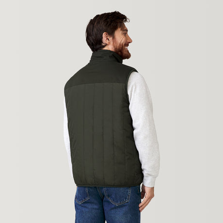 A man with brown hair and a beard wears the Clearance Men's FreeCycle® Alpine Reversible Vest in dark green over a light gray sweatshirt and blue jeans, facing away from the camera against a plain light background.
