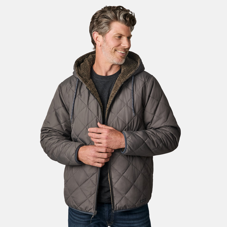 [Kolby is 6'2" wearing size M.] Men’s Free Country grey quilted hooded jacket with full-zip closure, adjustable drawstring hood, and dual hand pockets—reversible to a plush sherpa lining for enhanced warmth and cozy comfort. Styled over a dark crewneck and jeans for an effortlessly rugged, cold-weather vibe.