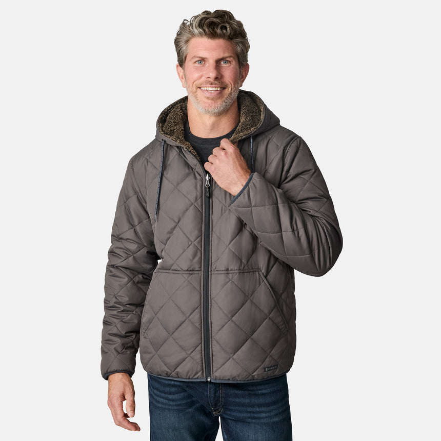[Kolby is 6'2" wearing size M.] Men’s Free Country grey quilted hooded jacket with full-zip closure, adjustable drawstring hood, and dual hand pockets—reversible to a plush sherpa lining for enhanced warmth and cozy comfort. Styled over a dark crewneck and jeans for an effortlessly rugged, cold-weather vibe.