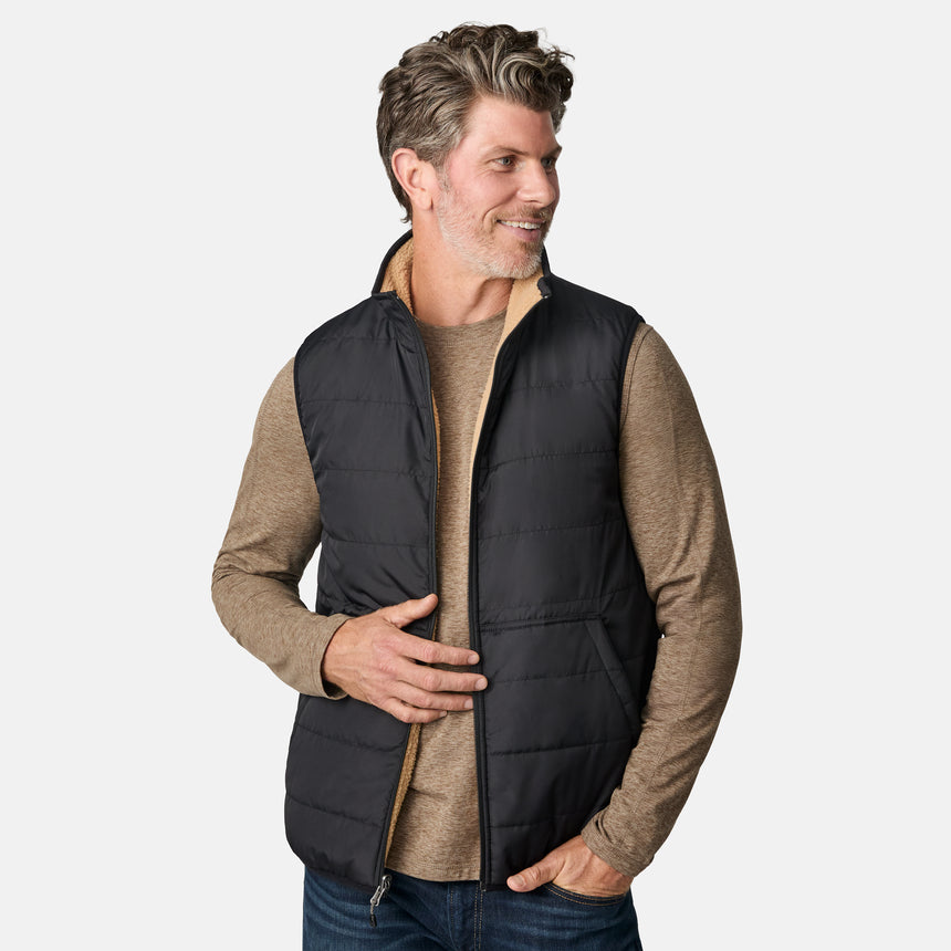 [Kolby is 6'2" wearing size M.] Free Country black quilted vest with zip-front closure and side pockets—worn over a beige long-sleeved shirt and blue jeans for a layered, transitional-weather look.
