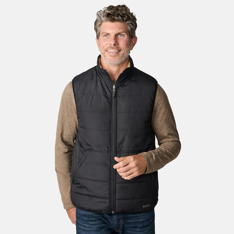 [Kolby is 6'2" wearing size M.] Free Country black quilted vest with zip-front closure and side pockets—worn over a beige long-sleeved shirt and blue jeans for a layered, transitional-weather look.