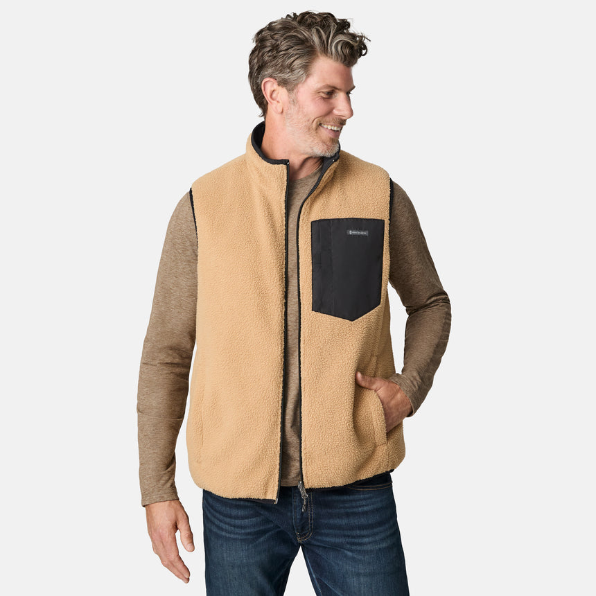 [Kolby is 6'2" wearing size M.] Free Country men's reversible black quilted vest with zip-front closure and side pockets—worn over a beige long-sleeved shirt and blue jeans for a layered, transitional-weather look.