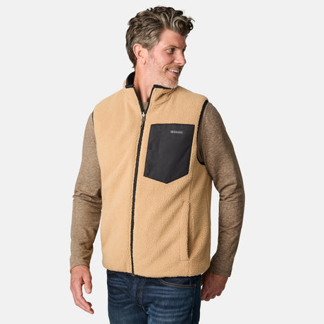 [Kolby is 6'2" wearing size M.] Free Country men's reversible black quilted vest with zip-front closure and side pockets—worn over a beige long-sleeved shirt and blue jeans for a layered, transitional-weather look.