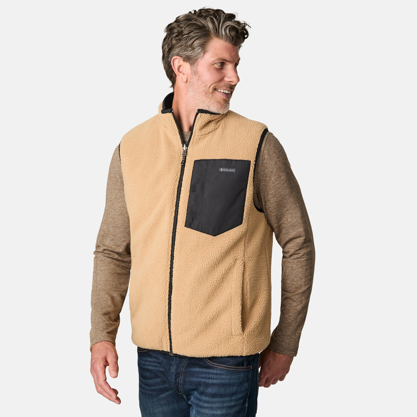 [Kolby is 6'2" wearing size M.] Free Country men's reversible black quilted vest with zip-front closure and side pockets—worn over a beige long-sleeved shirt and blue jeans for a layered, transitional-weather look.