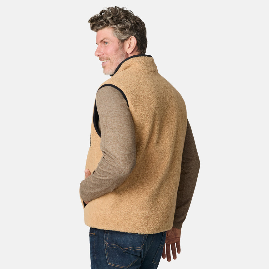 [Kolby is 6'2" wearing size M.] Free Country men's reversible black quilted vest with zip-front closure and side pockets—worn over a beige long-sleeved shirt and blue jeans for a layered, transitional-weather look.