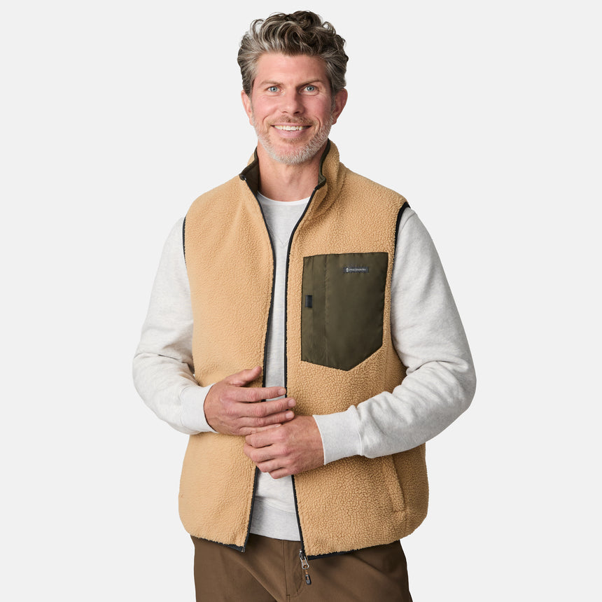 [Kolby is 6'2" wearing size M.] Men’s Free Country green quilted vest with zip-front closure and stand collar—reversible to tan sherpa fleece for versatile warmth and style. Shown layered over a light gray crewneck shirt with brown pants, styled for rugged, outdoor-ready appeal.