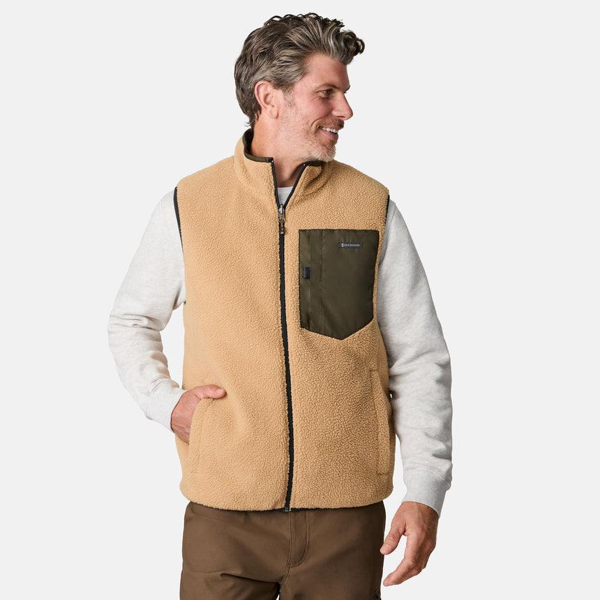 [Kolby is 6'2" wearing size M.] Men’s Free Country green quilted vest with zip-front closure and stand collar—reversible to tan sherpa fleece for versatile warmth and style. Shown layered over a light gray crewneck shirt with brown pants, styled for rugged, outdoor-ready appeal.