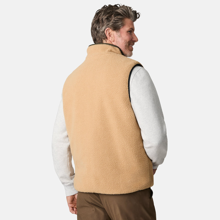 [Kolby is 6'2" wearing size M.] Men’s Free Country green quilted vest with zip-front closure and stand collar—reversible to tan sherpa fleece for versatile warmth and style. Shown layered over a light gray crewneck shirt with brown pants, styled for rugged, outdoor-ready appeal.