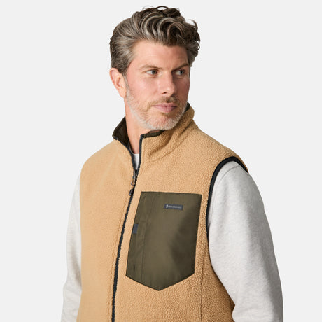 [Kolby is 6'2" wearing size M.] Men’s Free Country green quilted vest with zip-front closure and stand collar—reversible to tan sherpa fleece for versatile warmth and style. Shown layered over a light gray crewneck shirt with brown pants, styled for rugged, outdoor-ready appeal.