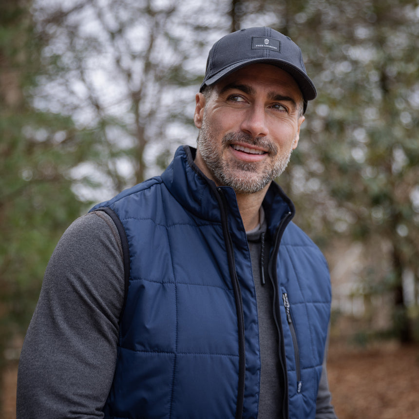 Man wearing a blue puffer vest and cap outdoors with trees in the background