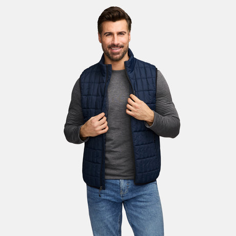 Male model wearing navy quilted full zip puffer vest over a gray long sleeve shirt.