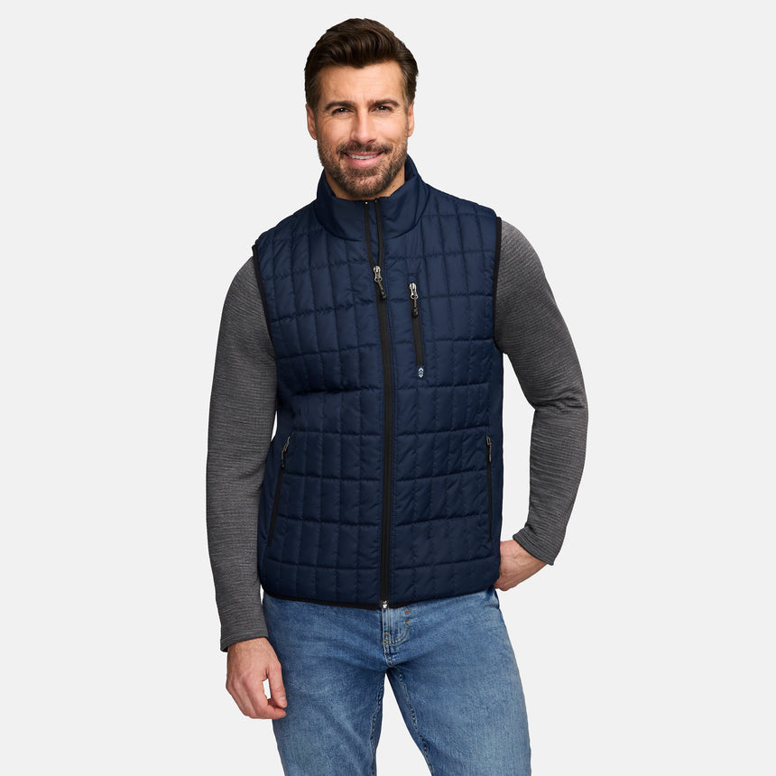 Man wearing a navy blue quilted full zip puffer vest over a gray long sleeve shirt.