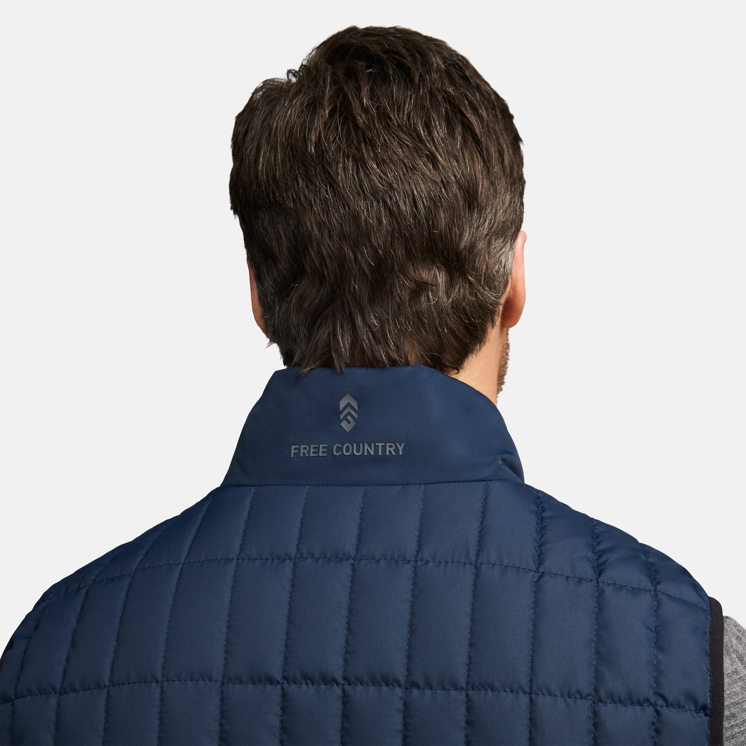 Back view of navy Sperrin full zip puffer vest on a person, with short dark hair and a collar logo.
