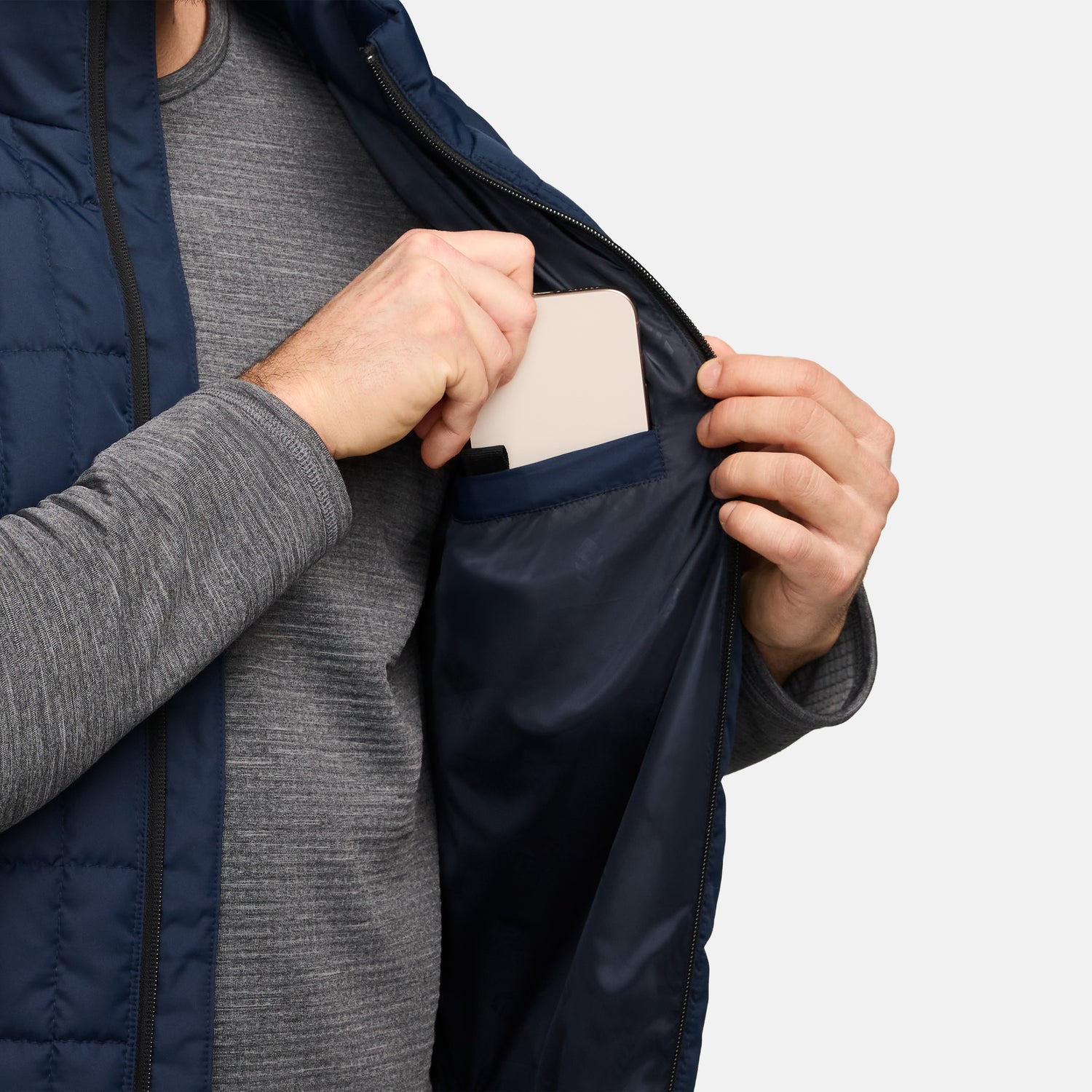 Person wearing navy Sperrin full zip puffer vest over a grey knit, holding a smartphone at chest level.