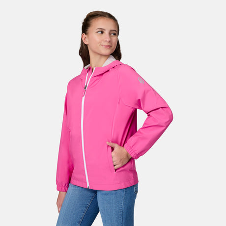 A girl models the Free Country Girls' Recess X2O Rain Jacket in bright pink, featuring a front zipper, paired with blue jeans, standing with one hand on her hip against a plain light background.