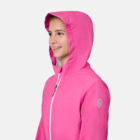 A young girl smiles and looks to the side, wearing the Free Country Girls' Recess X2O Rain Jacket in bright pink. The lightweight coat features a white zipper, a small sleeve logo, and is set against a plain white background.