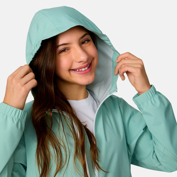 [Model is wearing a size Medium.] Girl wearing the Free Country Girls' Recess X2O Rain Jacket in Green Tea, size M, featuring lightweight stretch weatherproof fabric and a full length zipper and attached hood, paired with blue jeans #color_ green-tea