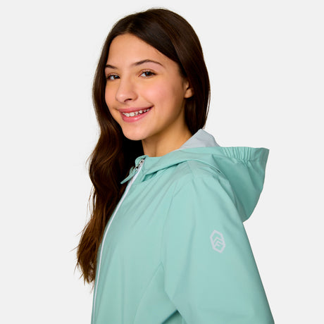 [Model is wearing a size Medium.] Girl wearing the Free Country Girls' Recess X2O Rain Jacket in Green Tea, size M, featuring lightweight stretch weatherproof fabric and a full length zipper and attached hood, paired with blue jeans #color_ green-tea
