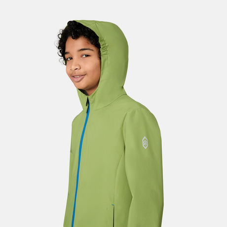A young person with curly hair stands sideways and smiles against a plain light background, wearing the Free Country Boys' Hydro Lite Recess X2O Rain Jacket in light green with a blue zipper.