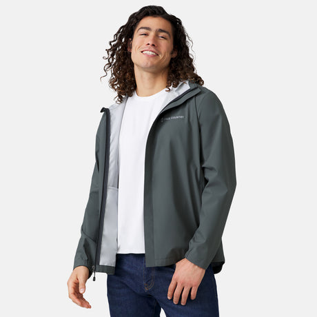 [Jordan is 6'2" wearing a size Medium.] Man wearing Free Country Men's Hydro Lite X2O Spectator Waterproof Jacket in Pewter, size M, made from lightweight four way stretch performance fabric featuring sealed seams, elastic cuffs, and an attached hood with a drawcord, styled with blue jeans #color_pewter