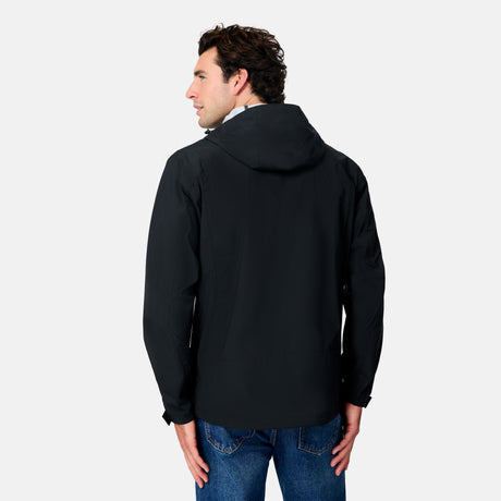 A man with dark hair, wearing the Free Country Men's Hydro Lite X2O Status Jacket in black and blue jeans, stands facing away with his head slightly turned to the left against a plain white background.