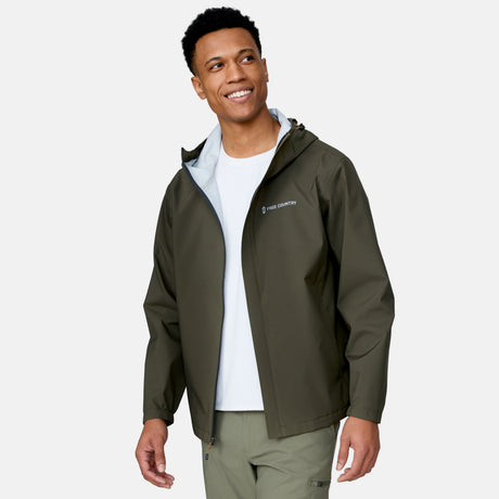 [Josiah is 6'3" wearing a size Medium.] Man wearing Free Country Men's Hydro Lite X2O Spectator Waterproof Jacket in Olive, size M, made from lightweight four way stretch performance fabric featuring sealed seams, elastic cuffs, and an attached hood with a drawcord, styled with green pants #color_olive