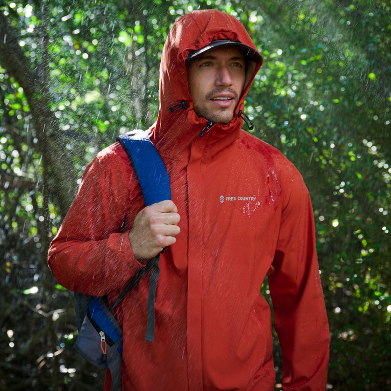 Man wearing a red raincoat with a blue backpack in a rainy forest setting