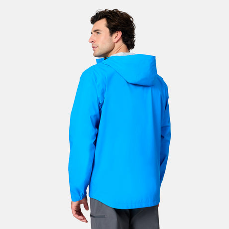 A man with short brown hair, dressed in gray pants, faces away and looks over his left shoulder while wearing the Free Country Men's Hydro Lite X2O Spectator Waterproof Jacket in bright blue against a plain light background.