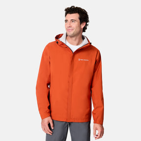 A man wears the Men's Hydro Lite X2O Spectator Waterproof Jacket by Free Country, a bright orange lightweight rain jacket, standing against a plain white background and smiling as he looks to the side.