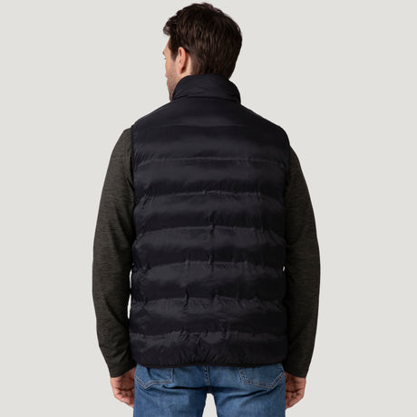 [Vince is 6'1" wearing a size Medium.] Man wearing the Free Country Men's Pine Creek Quilted Reversible Vest in black, featuring a quilted outer layer, cozy curly fleece reverse, and REPREVE® synthetic fill, styled with a black long-sleeve shirt and dark jeans.