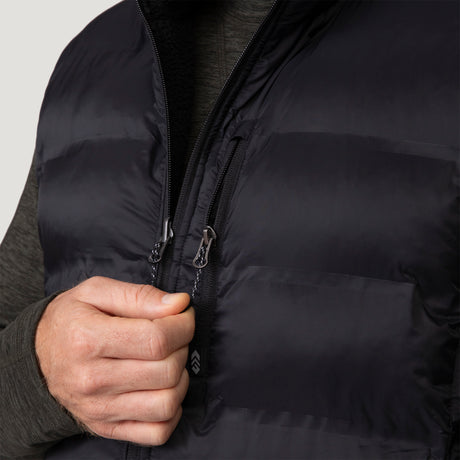 [Vince is 6'1" wearing a size Medium.] Man wearing the Free Country Men's Pine Creek Quilted Reversible Vest in black, featuring a quilted outer layer, cozy curly fleece reverse, and REPREVE® synthetic fill, styled with a black long-sleeve shirt and dark jeans.