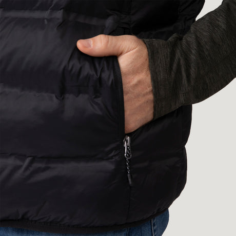 [Vince is 6'1" wearing a size Medium.] Man wearing the Free Country Men's Pine Creek Quilted Reversible Vest in black, featuring a quilted outer layer, cozy curly fleece reverse, and REPREVE® synthetic fill, styled with a black long-sleeve shirt and dark jeans.