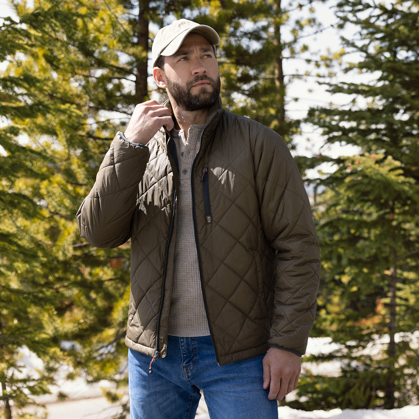 Man wearing a quilted jacket and cap in a forest setting