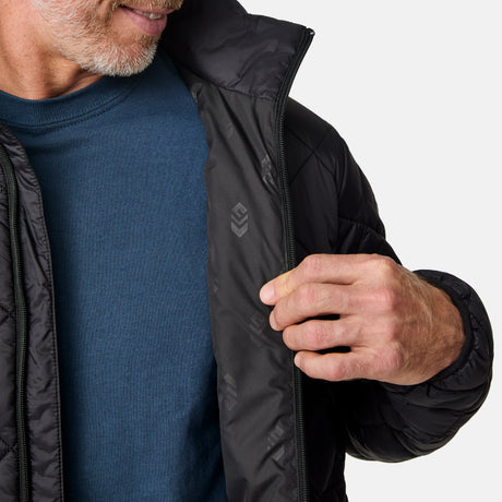 [Kolby is 6'2" wearing size M] Model wearing a black quilted Free Country jacket with diamond-pattern stitching, high stand collar, and zippered chest pocket; paired with brown pants and a blue crewneck tee for a warm, transitional-weather look.