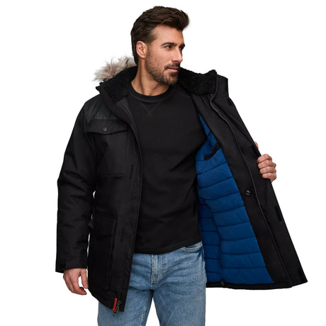 A man with short brown hair and a beard, dressed in a black shirt and blue jeans, holds open a Clearance Men's Momentum II Midweight Parka Jacket with a fur-lined detachable hood, blue inner lining, and poly-fill insulation.