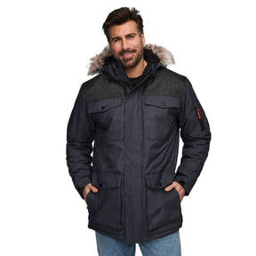 A man with short brown hair and a beard smiles with hands in pockets, wearing a Clearance Men's Momentum II Midweight Parka Jacket with detachable hood and faux fur trim, along with a black shirt and blue jeans.