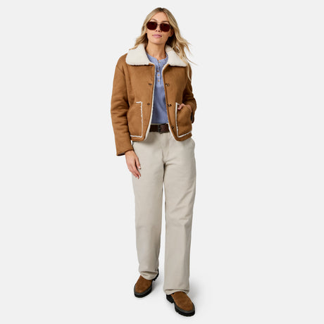 Woman wearing tan faux suede shearling reversible jacket with white sherpa trim and open front