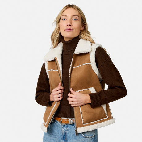 Woman wearing a brown faux suede shearling reversible vest with white trim over a brown knit sweater