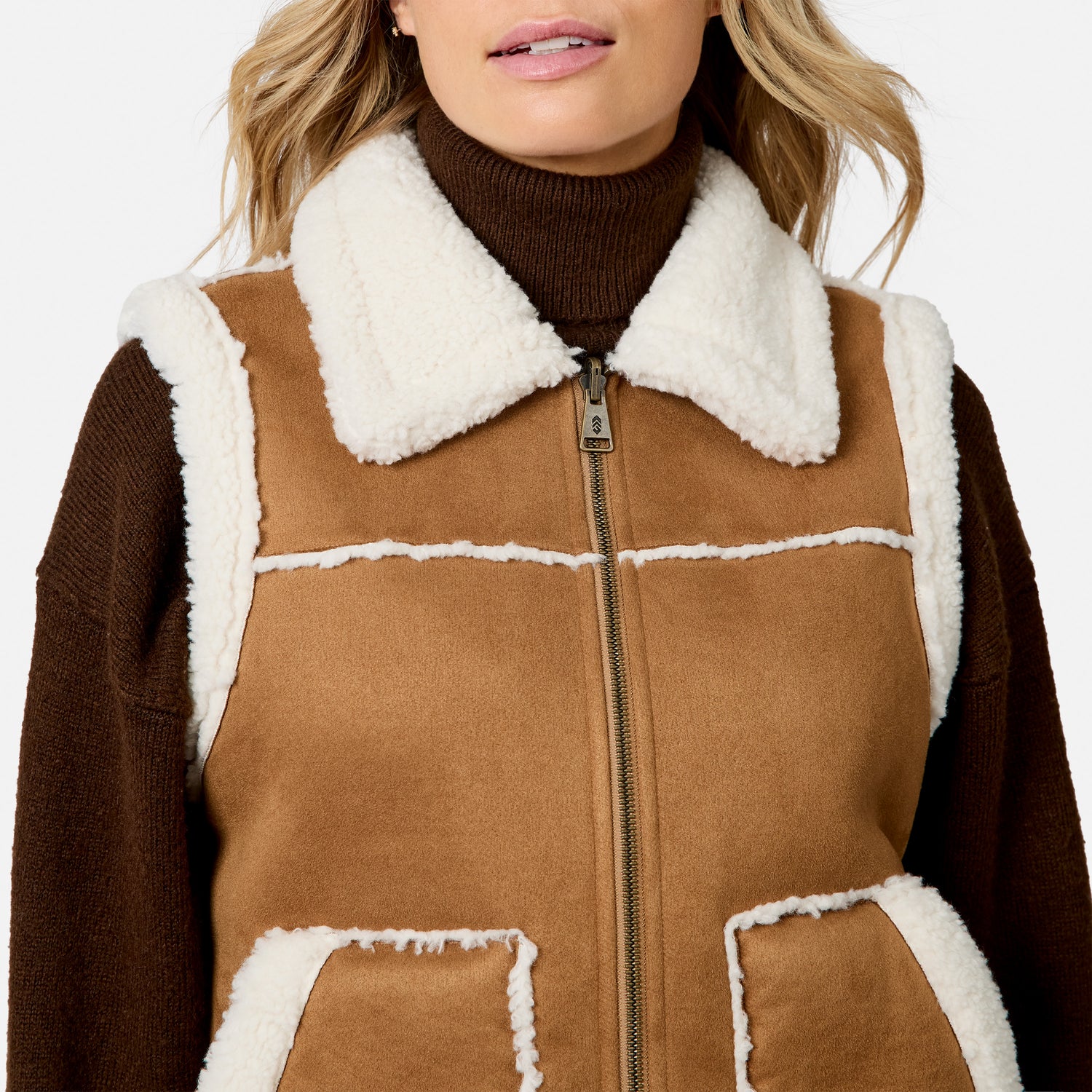 Close up of front zipper on tan brown faux suede shearling vest with white fleece trim