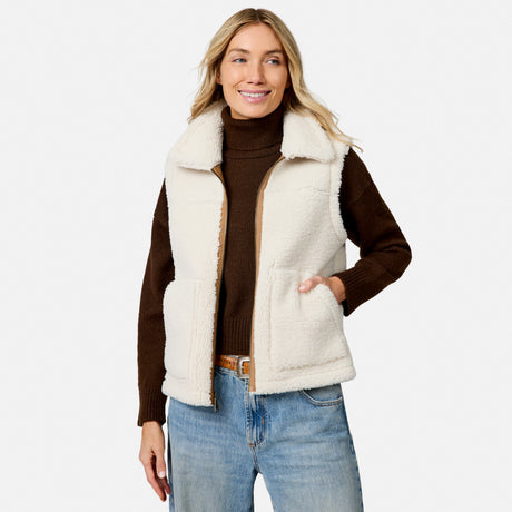 Woman wearing cream faux shearling reversible vest over a brown knit turtleneck