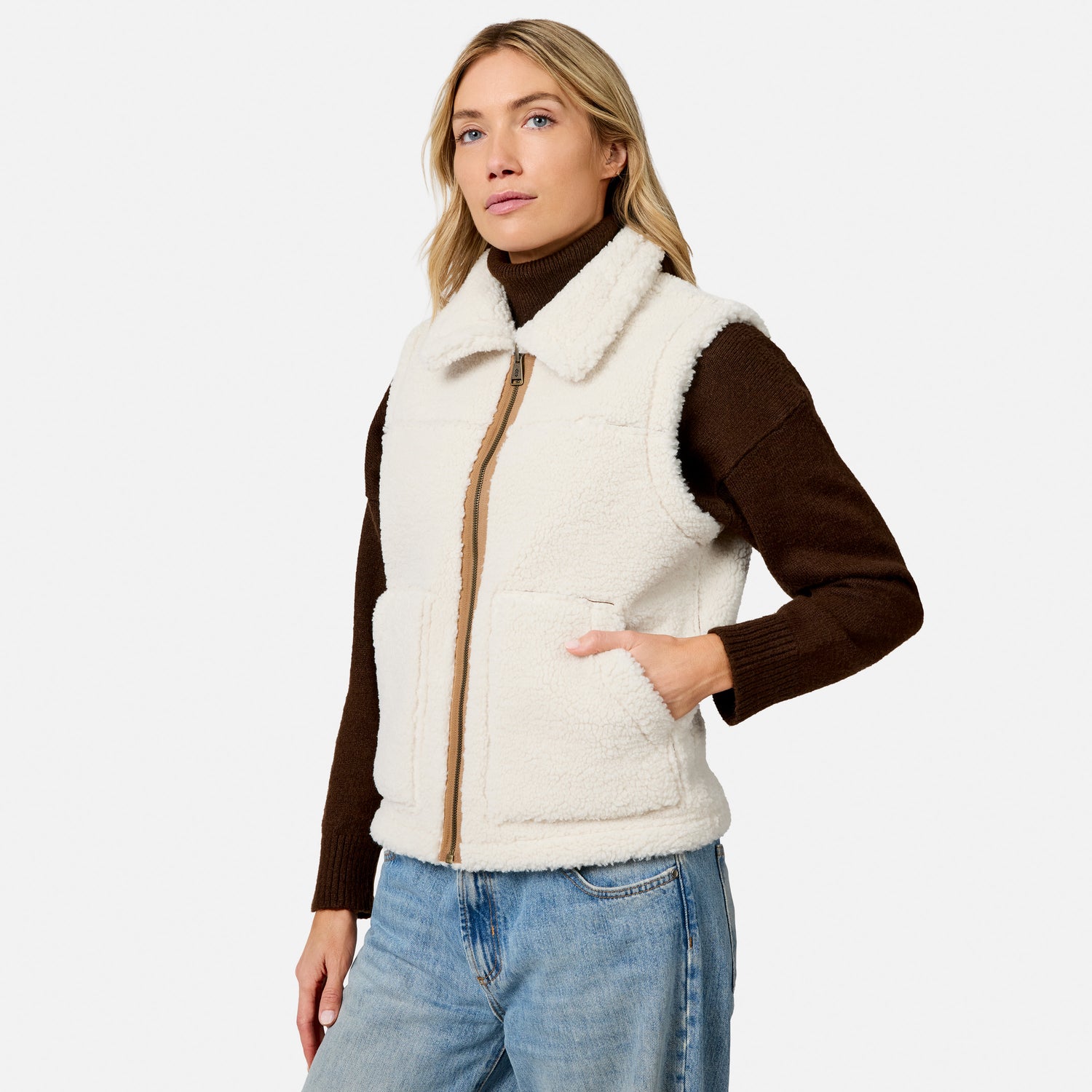 Model wearing ivory shearling vest with brown sleeves and zipper over a brown knit top