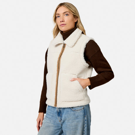 Model wearing ivory shearling vest with brown sleeves and zipper over a brown knit top