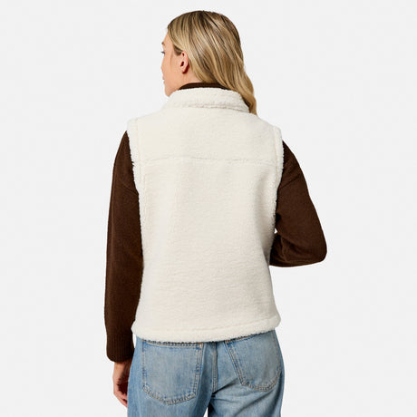 Back view of a woman wearing a cream faux shearling reversible vest with brown sleeves.