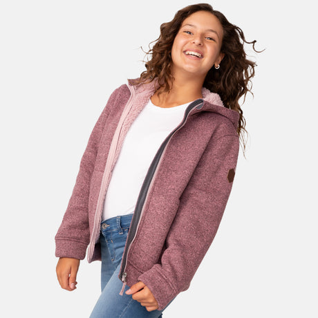 [Model is wearing size M.] Girl wearing the Free Country Girls' Mountain Fleece Jacket in textured pink, layered over a white shirt and blue jeans, smiling in a neutral-colored indoor setting.